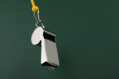 Photo of Referee equipment. Metal whistle on dark green background, closeup and space for text