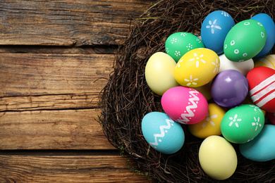 Photo of Colorful Easter eggs in decorative nest on wooden background, top view
