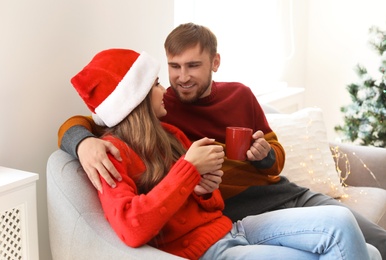 Photo of Happy young couple with cups of hot drink celebrating Christmas at home
