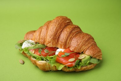 Photo of Tasty croissant with salmon, avocado, mozzarella and lettuce on green background, closeup