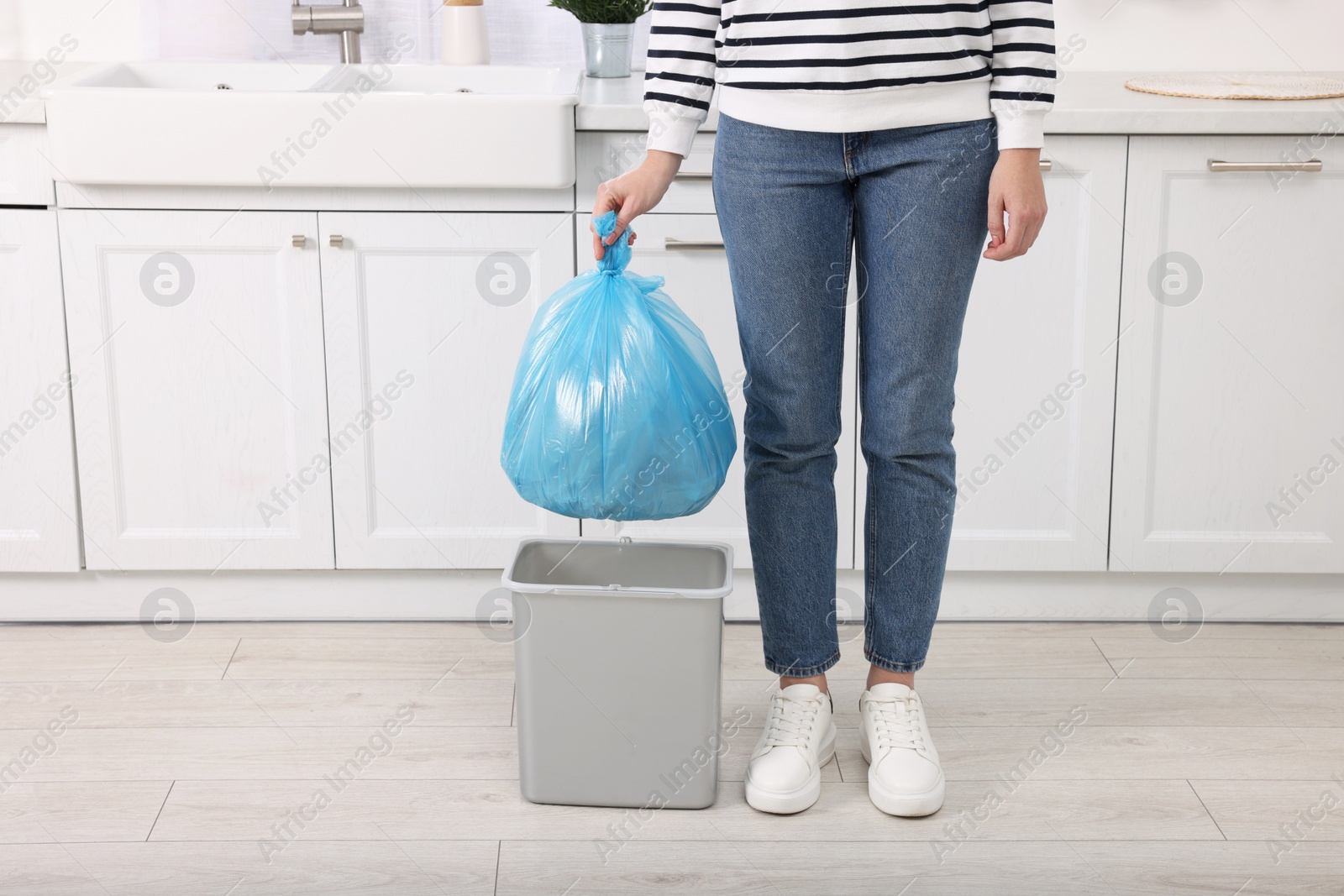 Photo of Woman taking garbage bag out of trash bin in kitchen, closeup