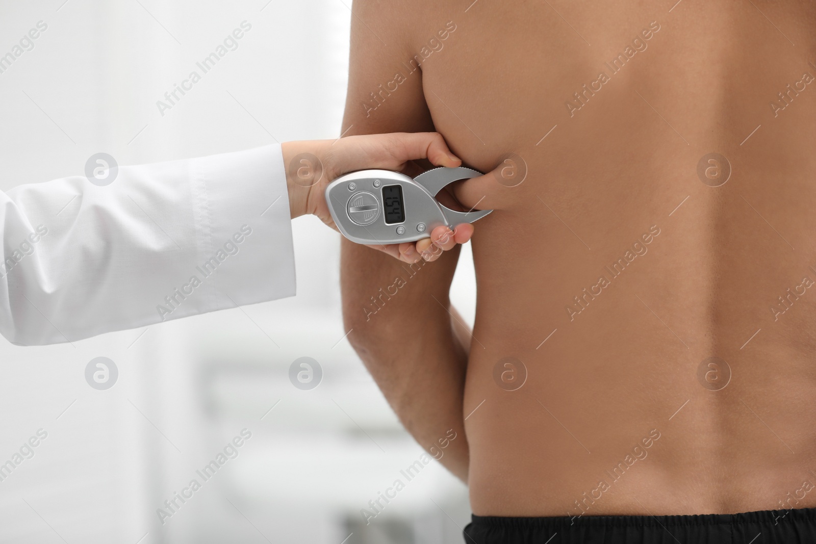 Photo of Nutritionist measuring man's body fat layer with digital caliper on blurred background, closeup