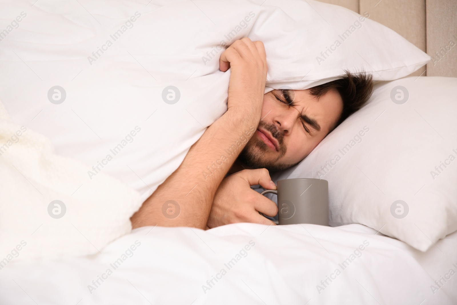 Photo of Sick young man with cup of hot drink in bed at home. Influenza virus