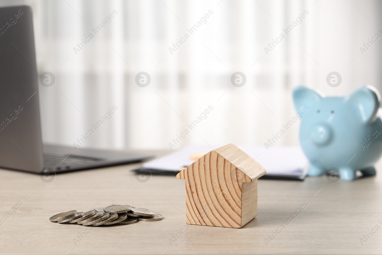 Photo of House model, coins, piggy bank and laptop on wooden table indoors, selective focus