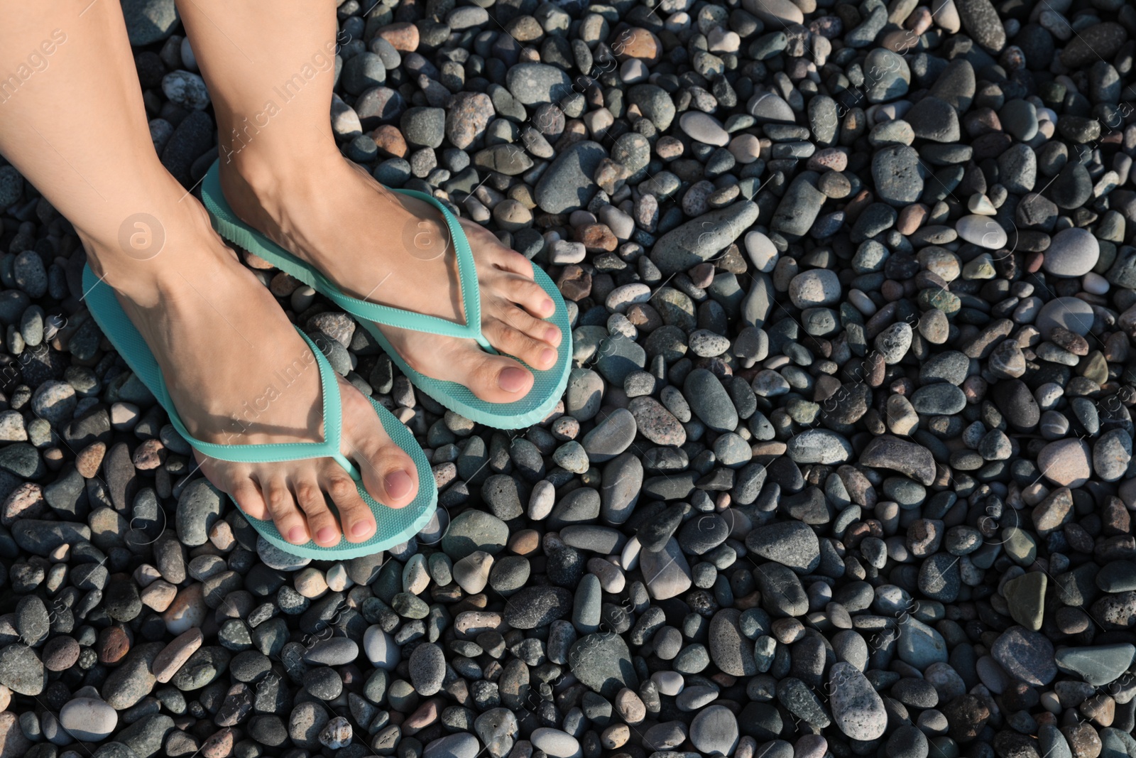 Photo of Woman in stylish flip flops on pebble beach, closeup. Space for text