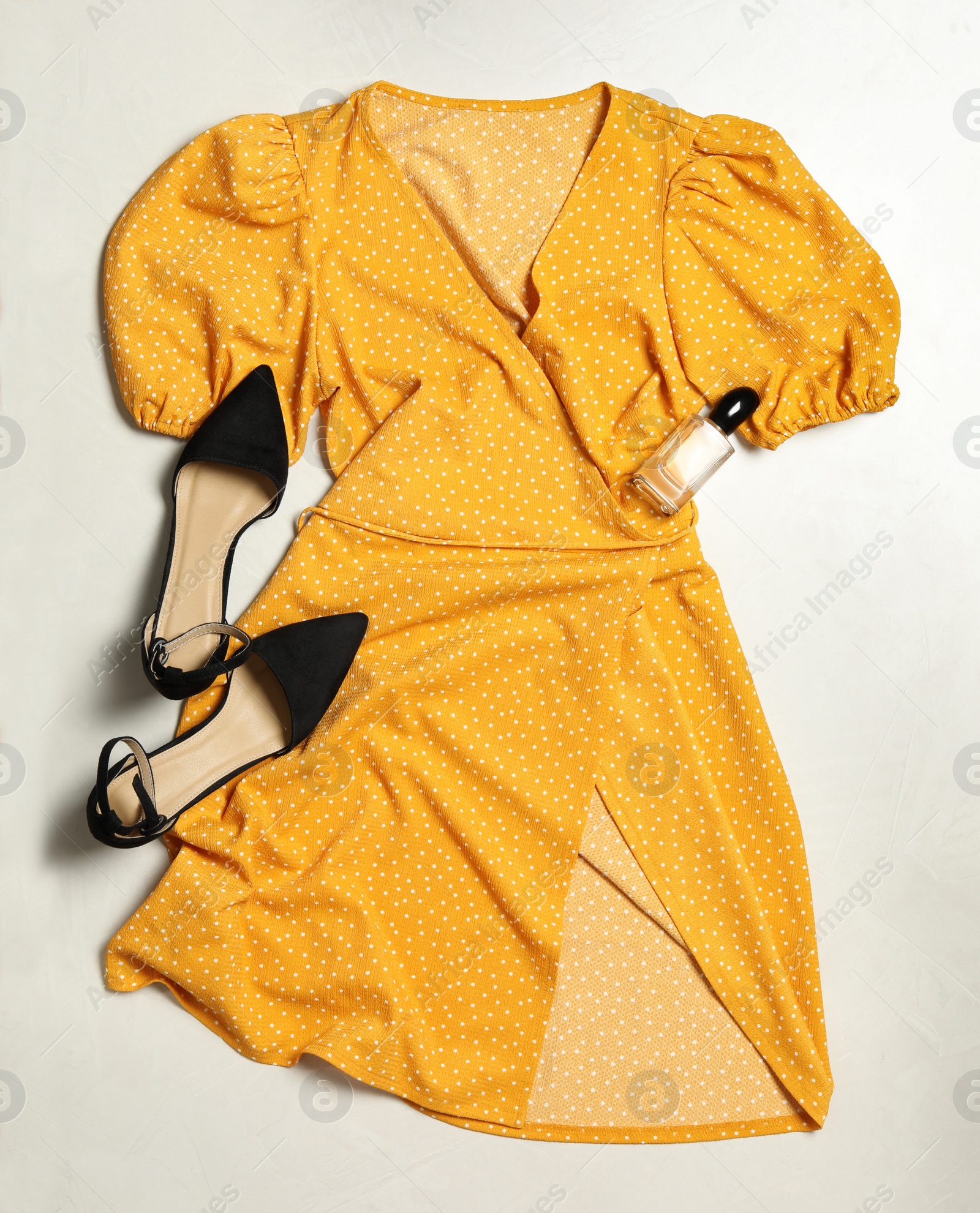 Photo of Stylish yellow dress, perfume and shoes on wooden floor, flat lay