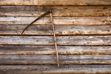 Photo of Scythe hanging on wooden wall. Agricultural tool