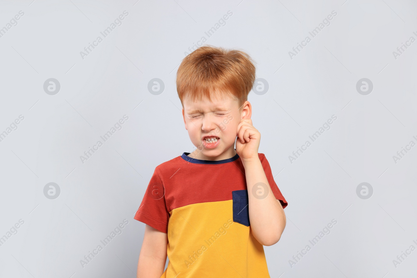 Photo of Little boy suffering from ear pain on light grey background