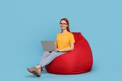 Smiling young woman with laptop sitting on beanbag chair against light blue background