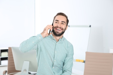 Photo of Young man laughing while talking on phone in office