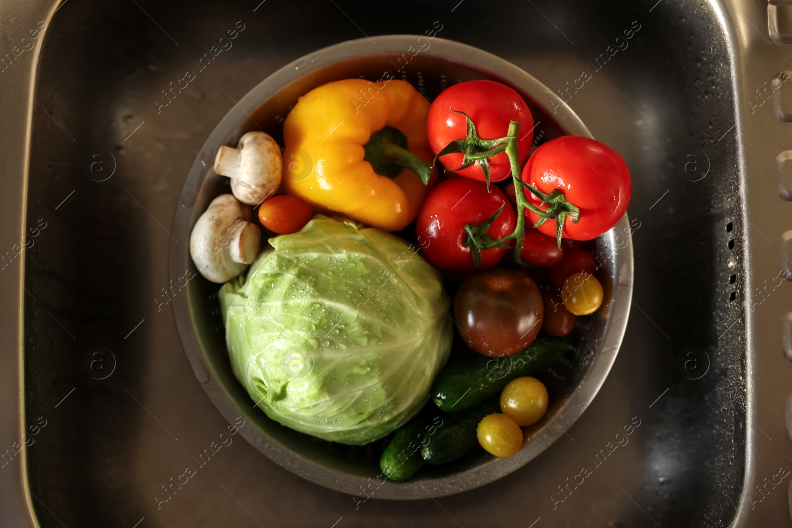 Photo of Different wet vegetables in metal colander inside sink, top view