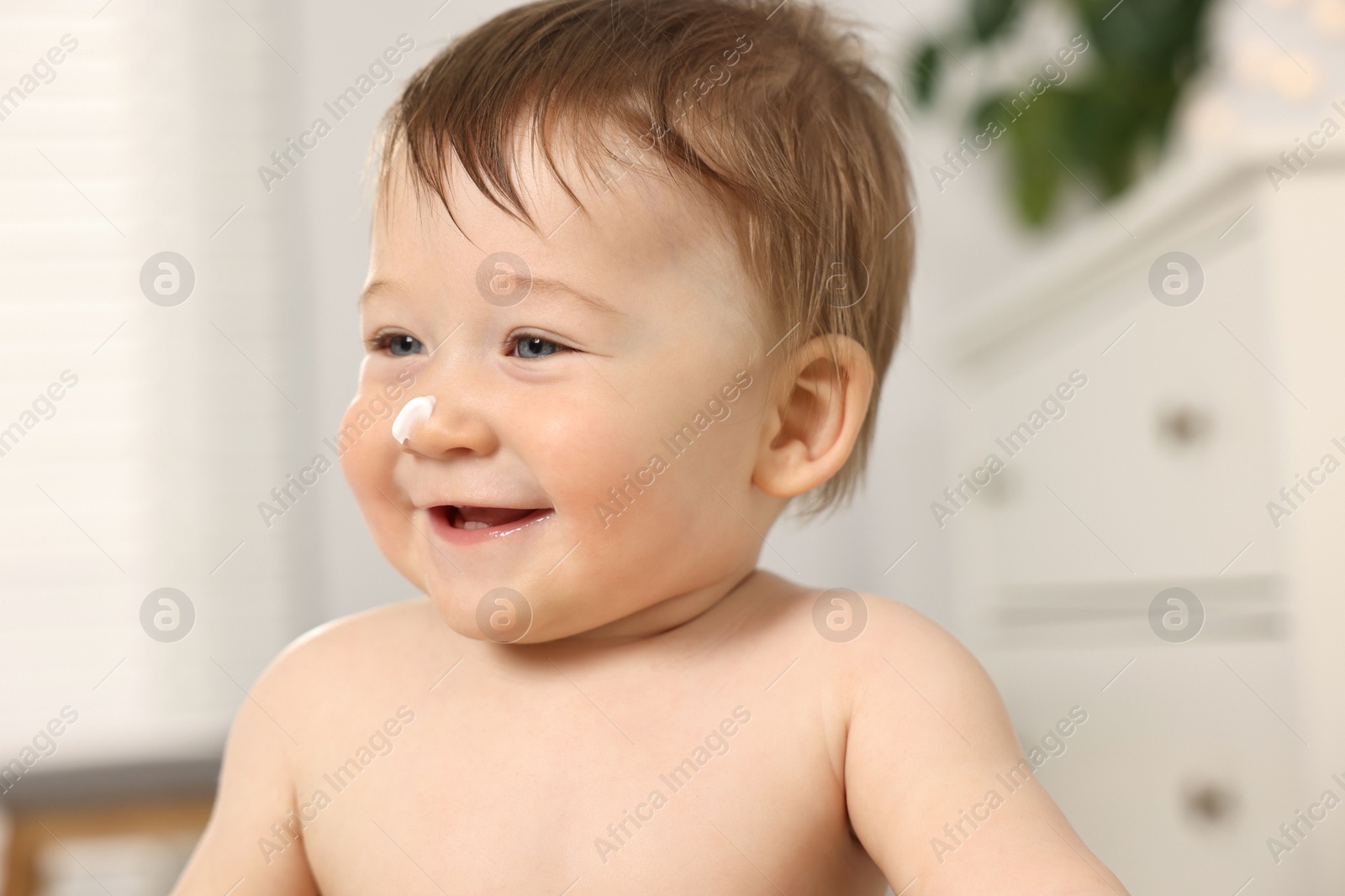 Photo of Cute little baby with moisturizing cream on face indoors