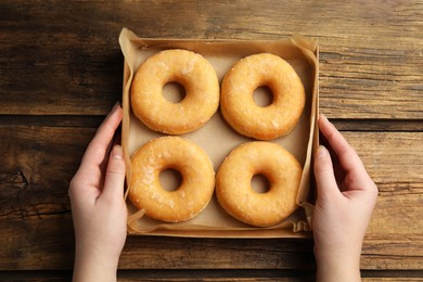 Photo of Woman with box of delicious donuts at wooden table, top view