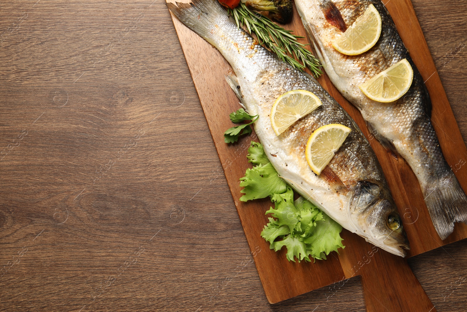 Photo of Delicious baked fish and vegetables on wooden table, top view. Space for text