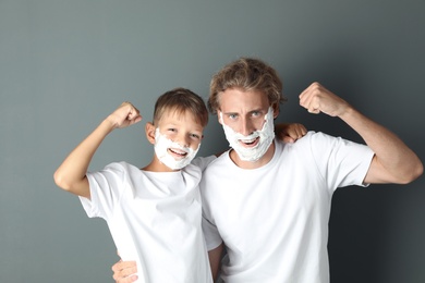 Photo of Father and son with shaving foam on faces against color background