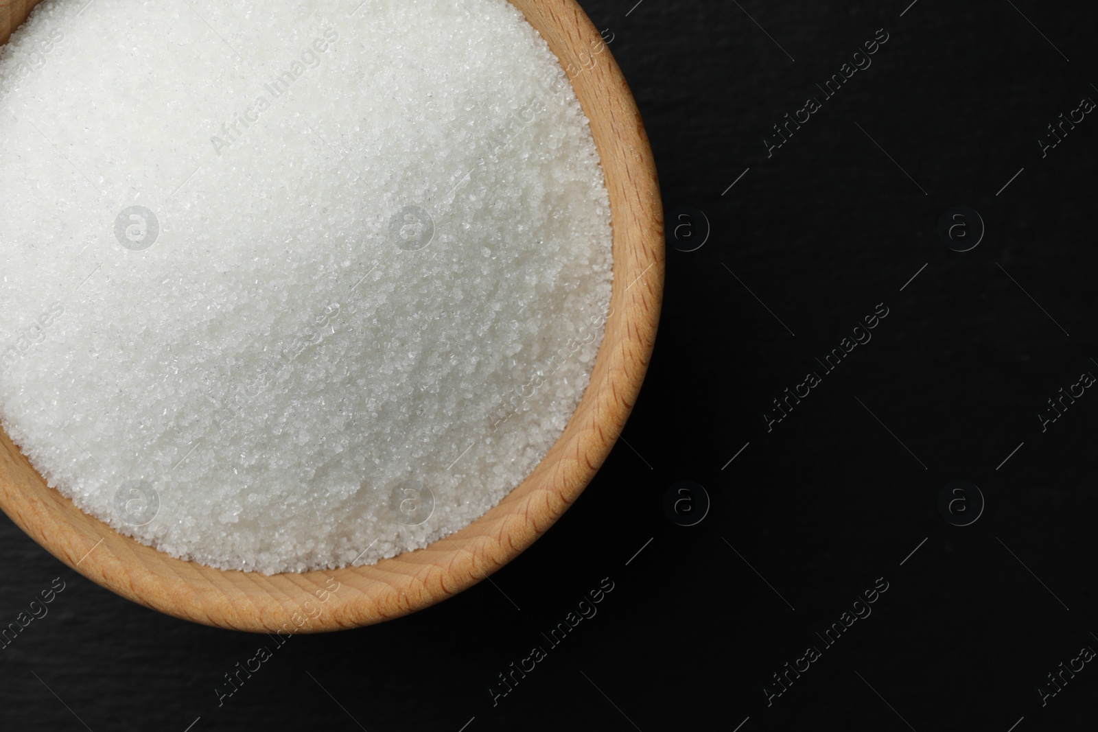 Photo of Granulated sugar in bowl on black table, top view. Space for text