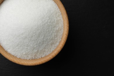 Granulated sugar in bowl on black table, top view. Space for text