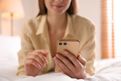 Young woman using modern smartphone on bed at home, closeup