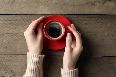 Photo of Woman holding cup of aromatic coffee at wooden table, top view