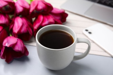 Photo of Cup of coffee and beautiful tulips near smartphone on light gray table, closeup