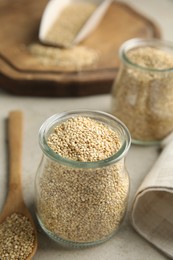 Photo of Jar and wooden spoon with white quinoa on light grey table. Space for text