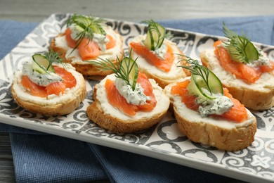 Tasty canapes with salmon, cucumber, cream cheese and dill on table, closeup