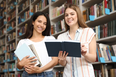 Photo of Young women with books near shelves in library