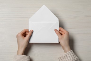 Photo of Woman holding letter envelope with card at light wooden table, top view