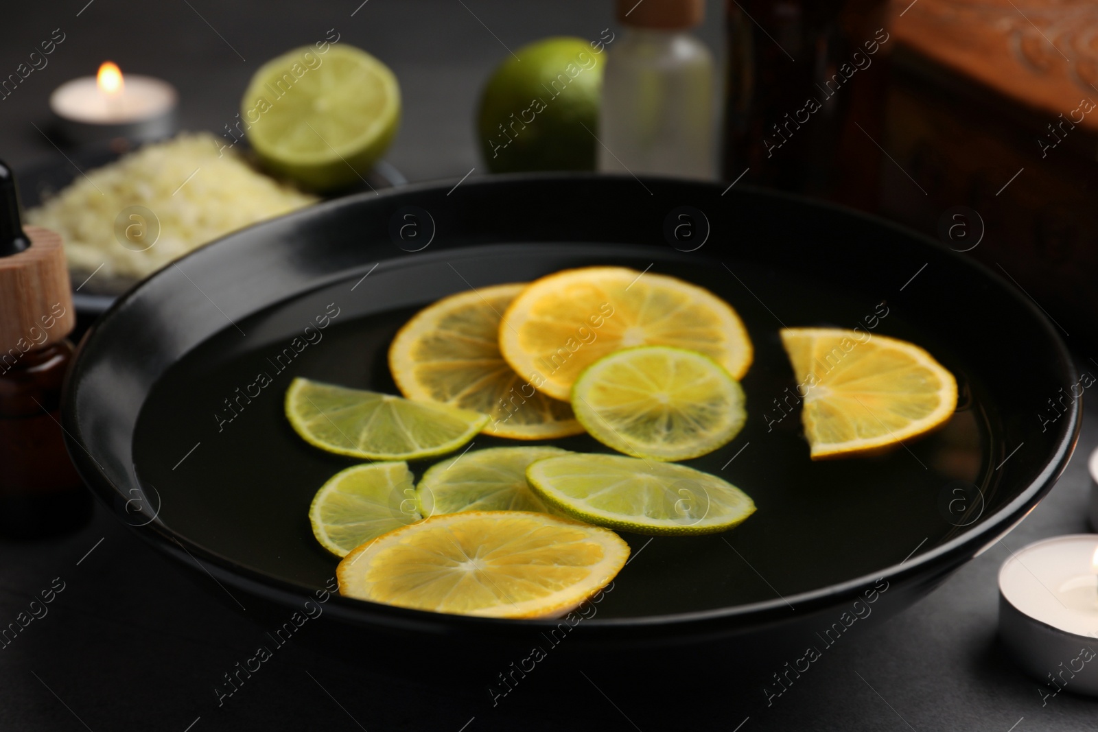 Photo of Bowl of essential oil and lemons on grey table, closeup. Aromatherapy treatment