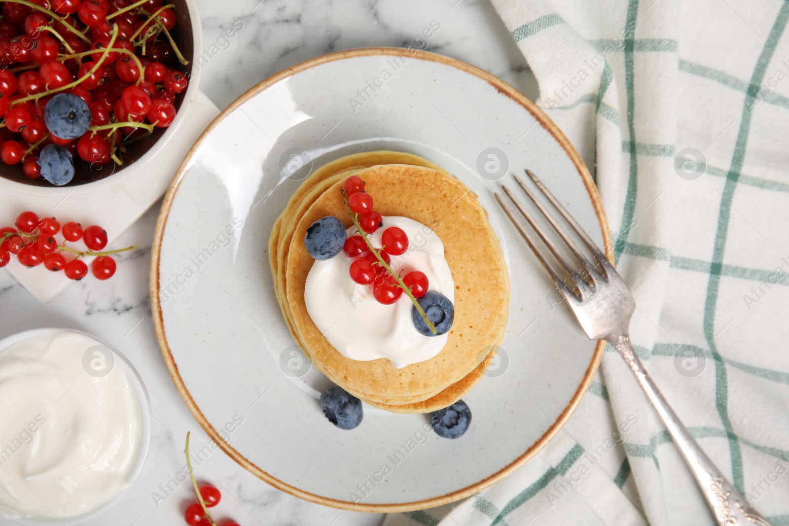 Photo of Pancakes with natural yogurt, blueberries and red currants on white marble table, flat lay