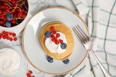 Pancakes with natural yogurt, blueberries and red currants on white marble table, flat lay