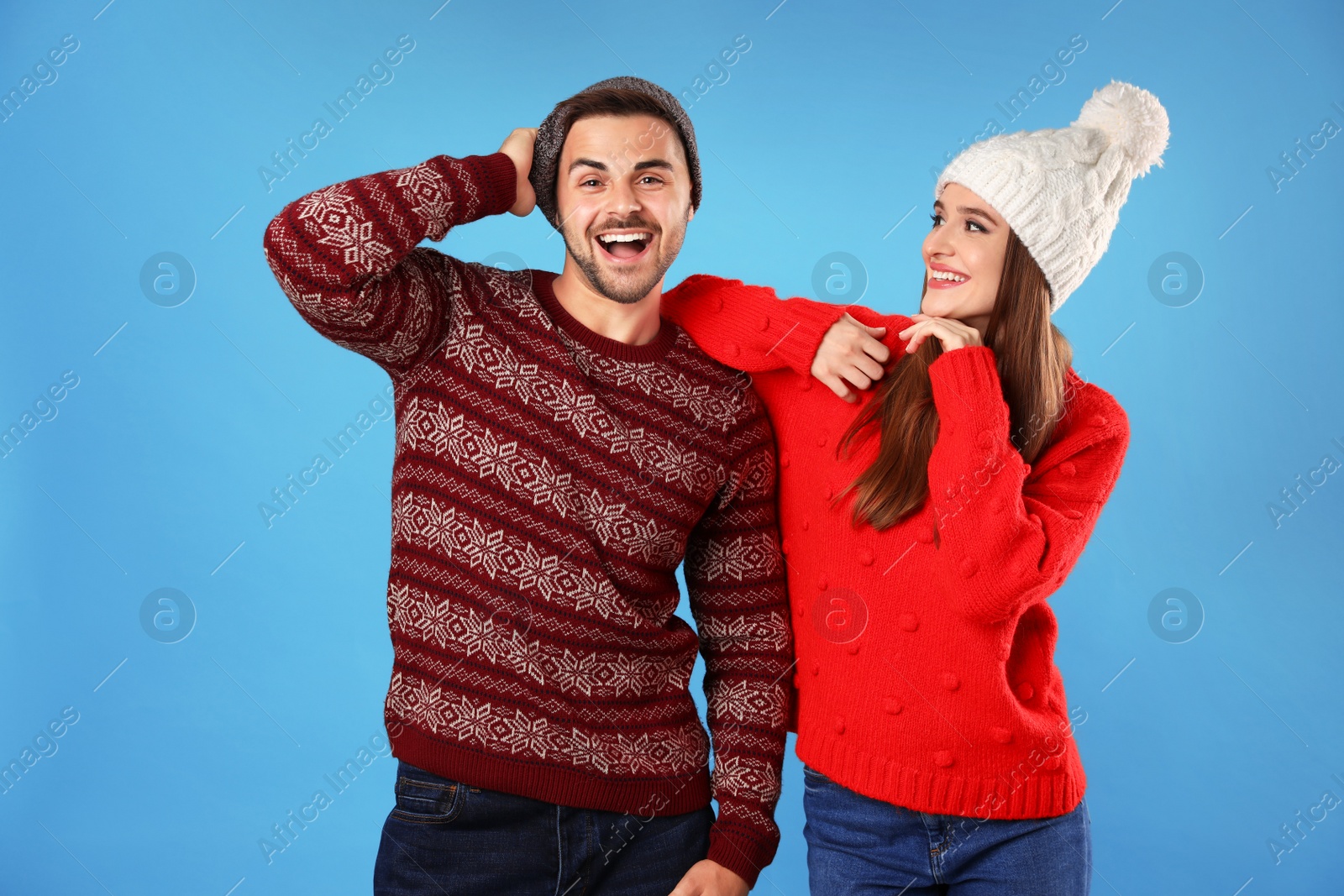 Photo of Couple wearing Christmas sweaters and hats on blue background