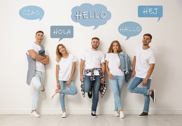 Happy people posing near light wall and illustration of speech bubbles with word Hello written in different languages