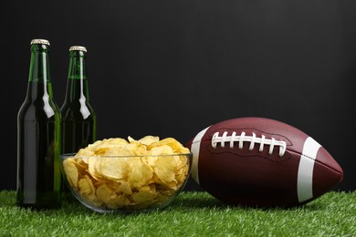 Photo of American football ball with potato chips and beer on green grass
