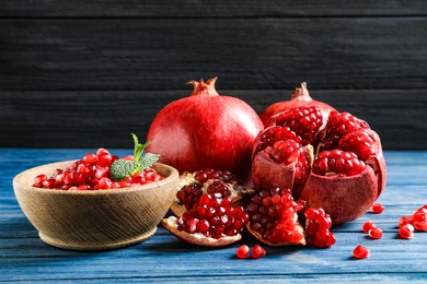 Photo of Bowl with seeds and ripe pomegranates on table against dark background