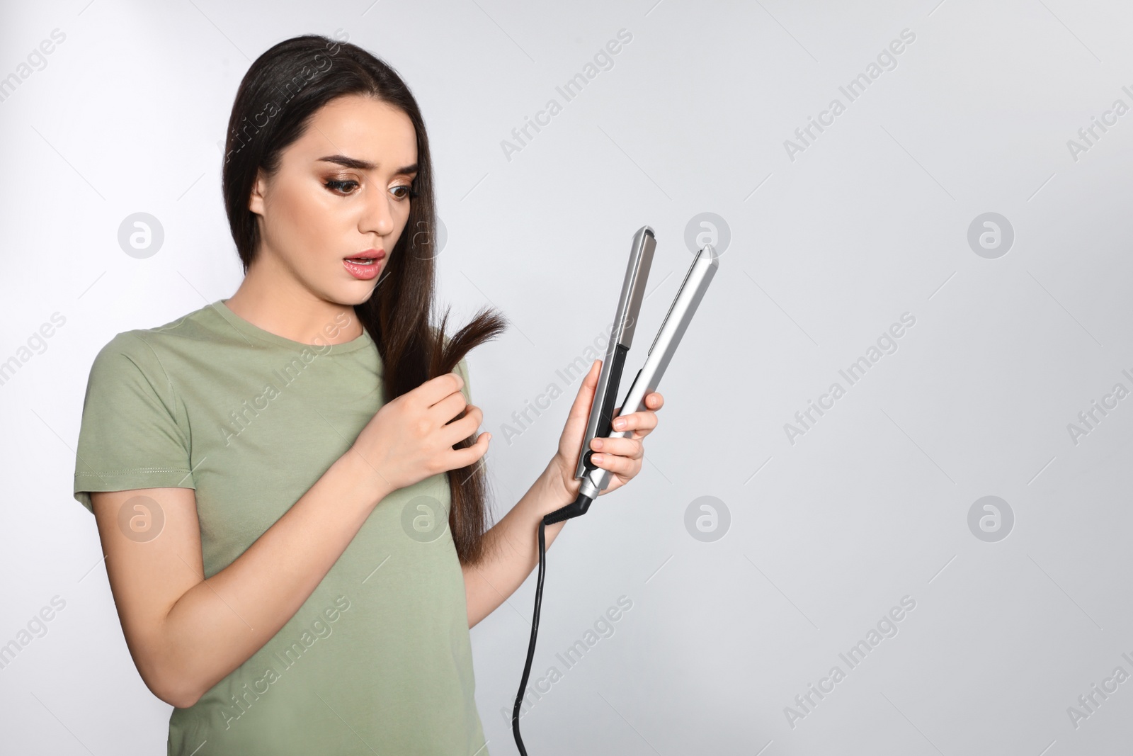 Photo of Emotional woman with hair iron on grey background. Space for text