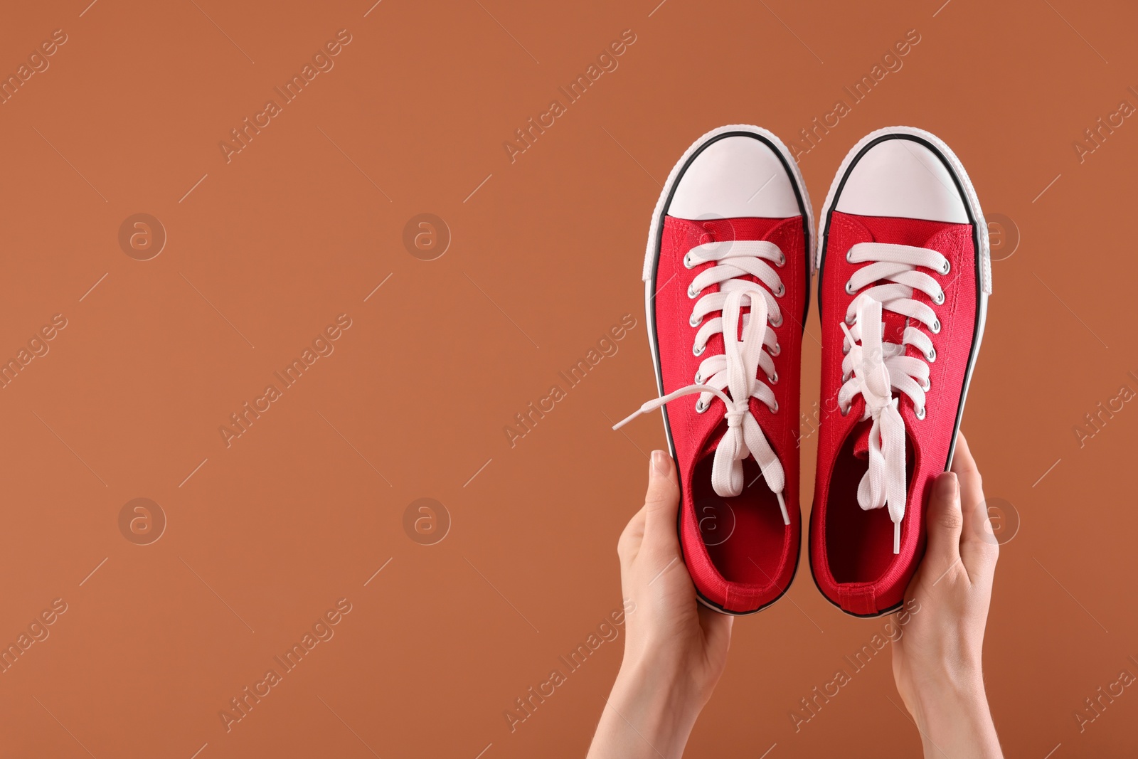 Photo of Woman with red classic old school sneakers on brown background, closeup. Space for text