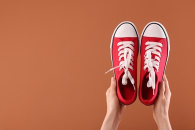 Woman with red classic old school sneakers on brown background, closeup. Space for text