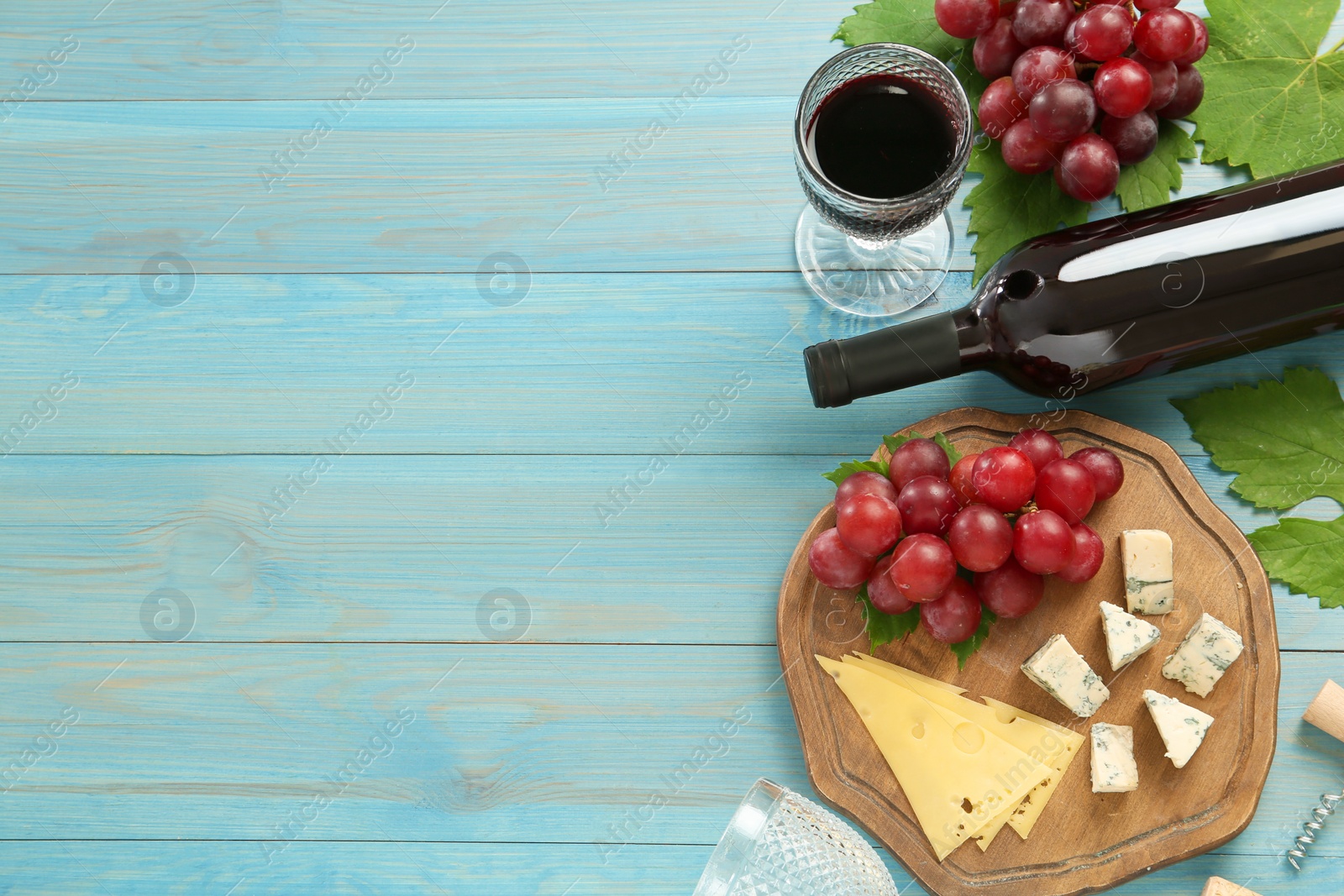 Photo of Tasty red wine and snacks on light blue wooden table, flat lay. Space for text