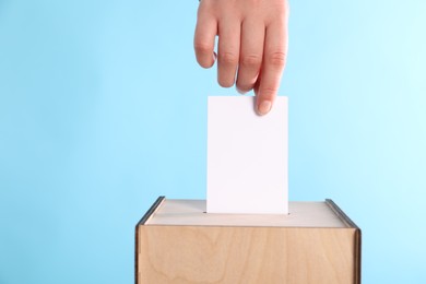 Photo of Woman putting her vote into ballot box on light blue background, closeup