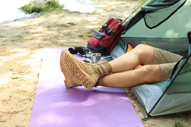 Young man resting in camping tent on riverbank, closeup. Space for text