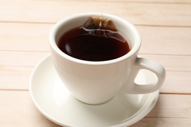 Photo of Tea bag and cup of hot beverage on light wooden table, closeup