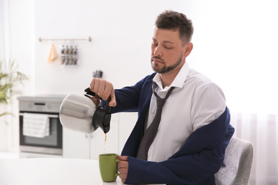 Photo of Sleepy man pouring coffee into cup at home in morning