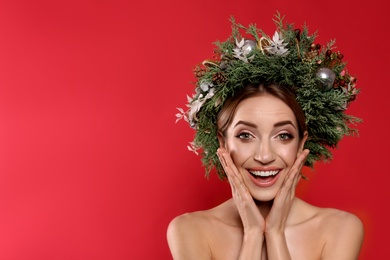 Emotional young woman wearing Christmas wreath on red background. Space for text