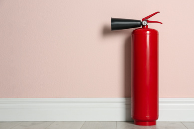 Photo of Fire extinguisher near pink wall indoors, space for text