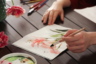 Woman painting flowers with watercolor at wooden table, closeup. Creative artwork