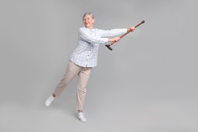 Senior woman with walking cane on gray background