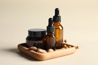 Wooden tray with bottles of cosmetic serum, jar and stones on beige background