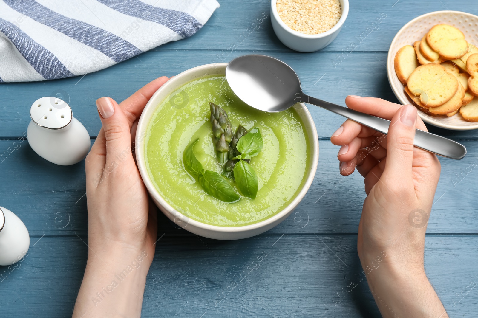 Photo of Woman eating delicious asparagus soup at blue wooden table, top view