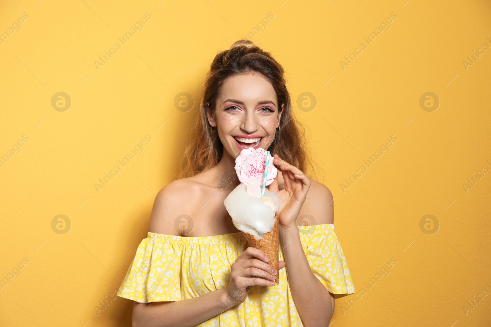Photo of Portrait of young woman holding cotton candy dessert on yellow background